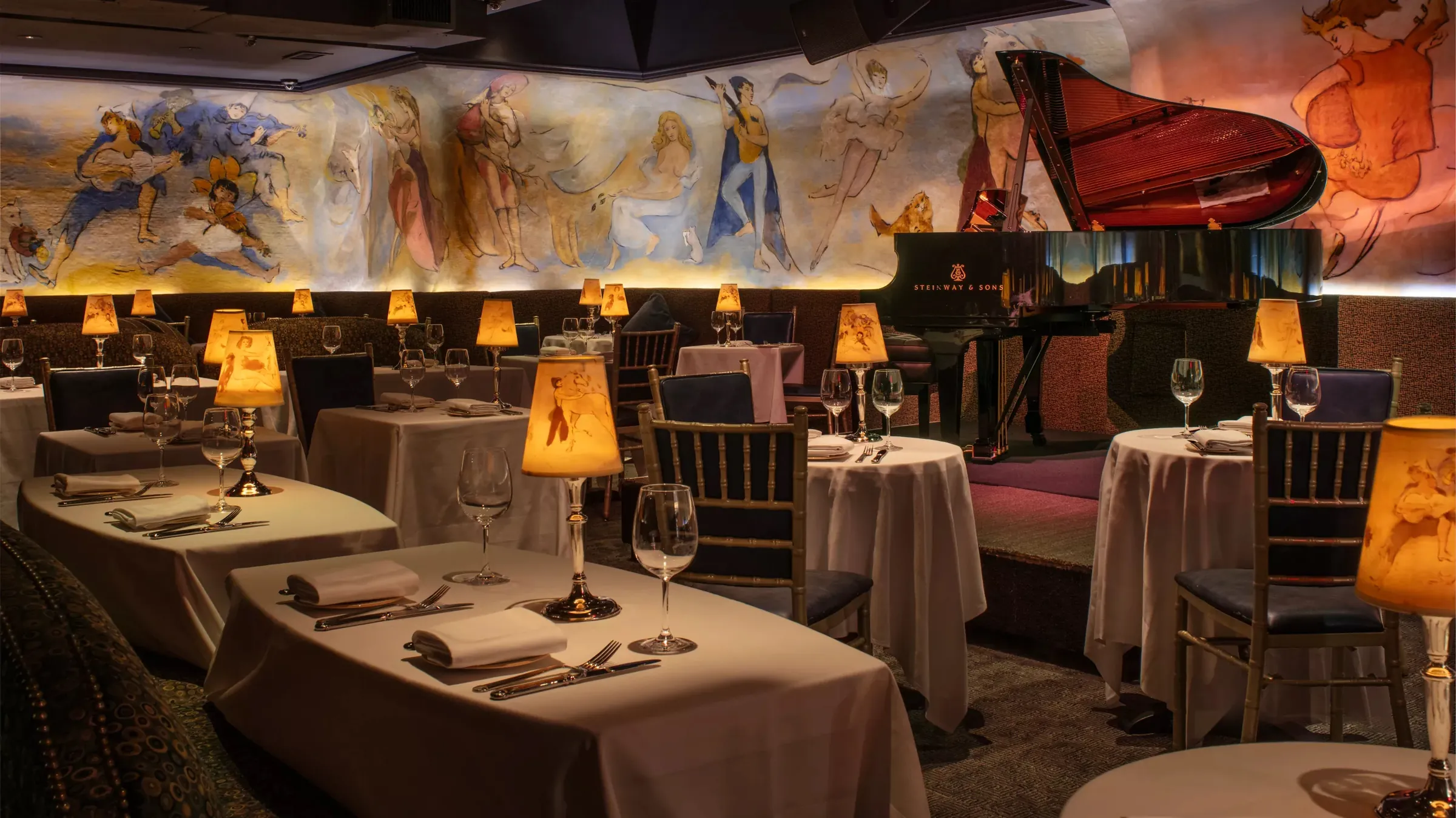 Lamplit tables and a grand piano beneath the painted murals at Bemelmans Bar