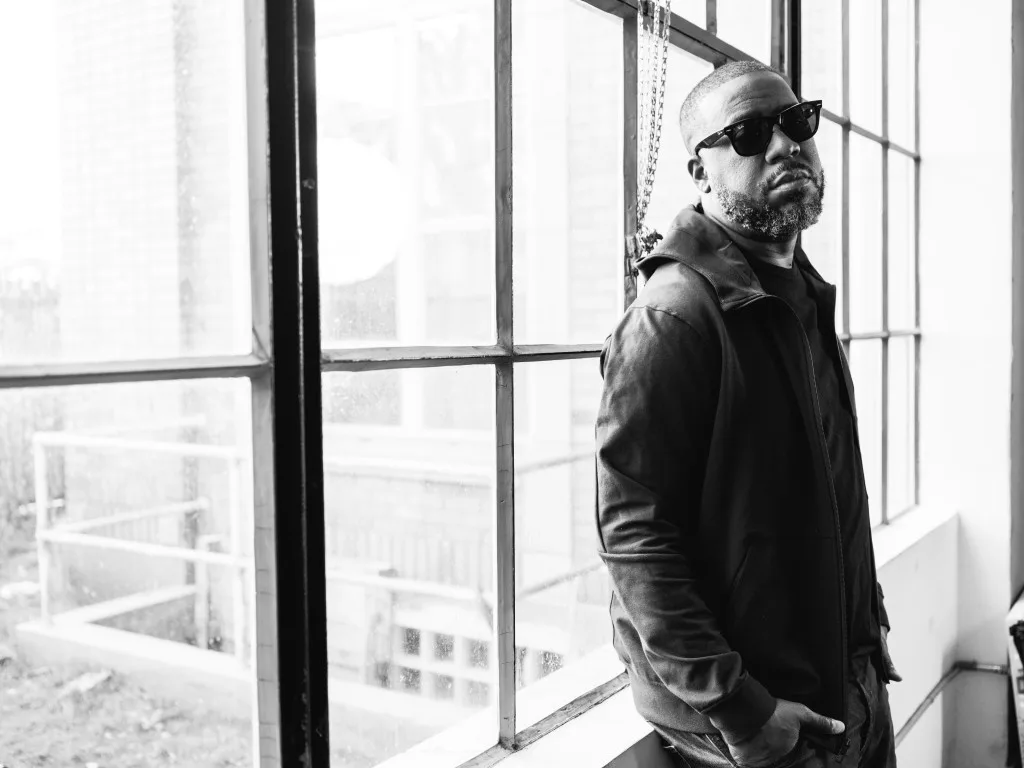Robert Glasper by a tall window, in black and white