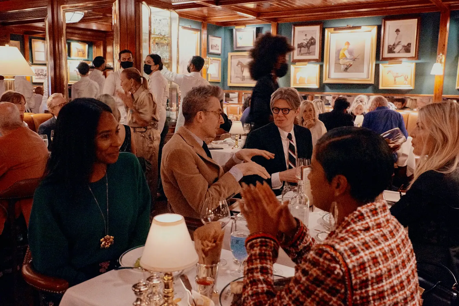 Diners at lamplit tables beneath equestrian paintings in The Polo Bar's dining room